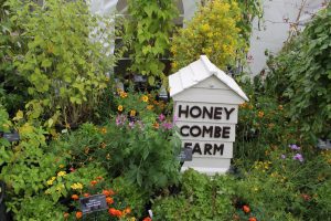 Vegetable display in full flower with a white wooden beehive in the centre; the beehive has the words 'honey combe farm' on it.