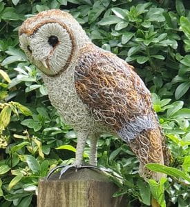 Barn owl made of wire sitting on a tree trunk.