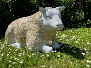 Large stone sheep on grass covered with daisies.